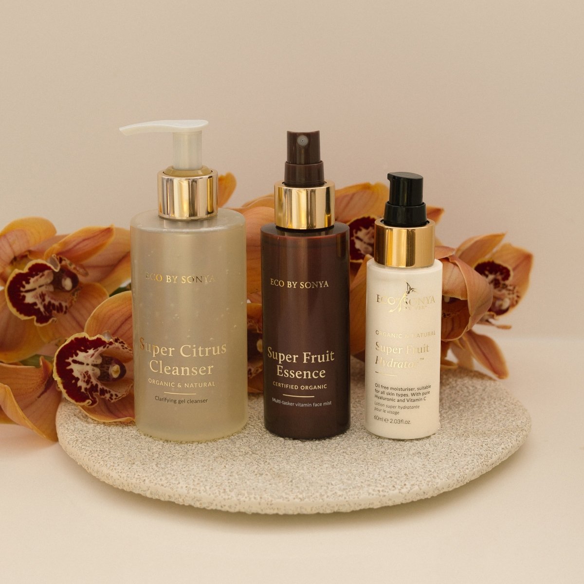 Eco By Sonya 3 step skincare system with Super Citrus Cleanser, Super Fruit Essence and Super Fruit Hydrator on a decorative plate with flowers in the background