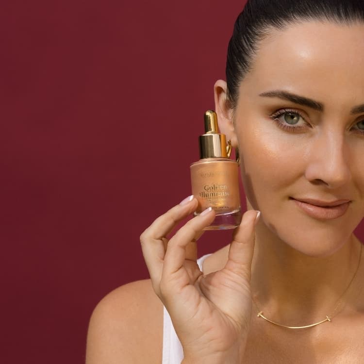 A woman holding a bottle of Eco By Sonya Golden Illuminiser - a sheer, luminous glow for face and body.