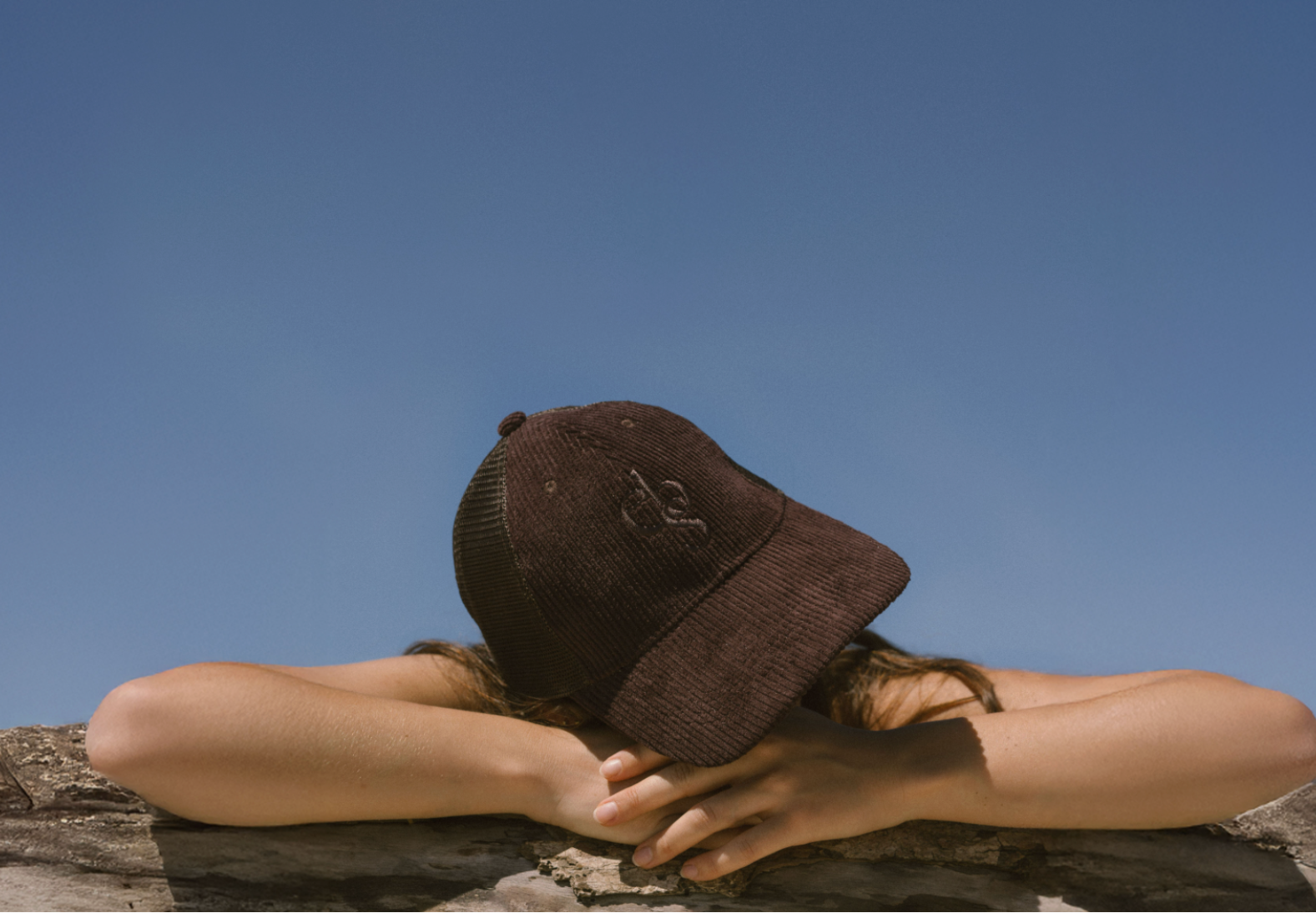 Person wearing a Eco By Sonya Good Thought Cap on a log with a clear blue sky in the background