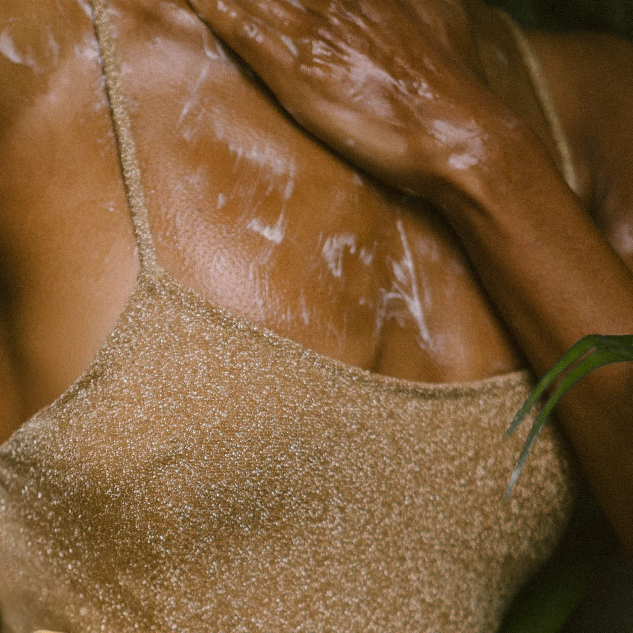 Close-up of a model wearing a gold glitter swimsuit top and applying ECO BY SONYA Body Wash