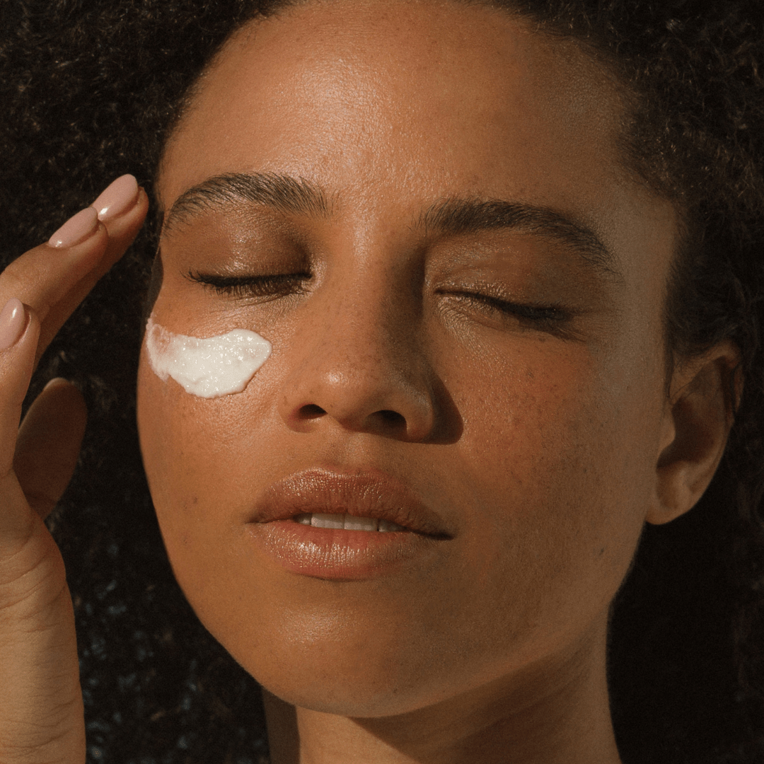 Close-up of woman applying Eco By Sonya Glory Cream to her cheek, showing rich creamy texture and hydrated smooth skin with a relaxed expression.