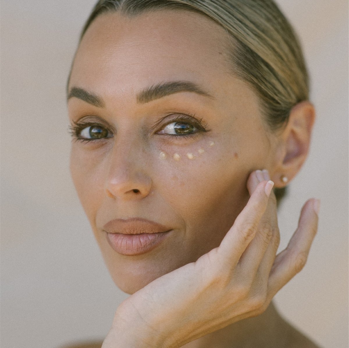 Close-up of a woman with three dots of Eco By Sonya Glory Eyes under her eye.