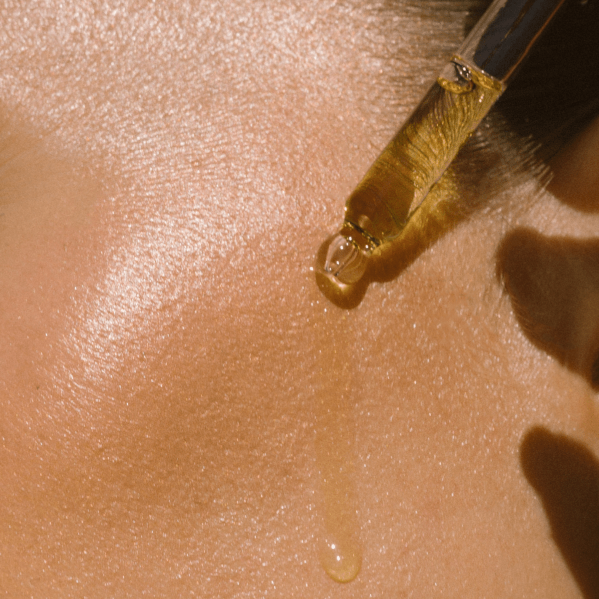 Close-up of dropper releasing a drop of Eco By Sonya Glory Oil onto smooth hydrated skin, showing rich golden oily texture and glow.