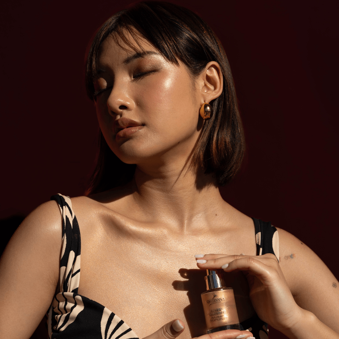 Woman with radiant golden skin holding Eco By Sonya Golden Illuminiser bottle near her body, showing luminous glow and sunlit radiance.
