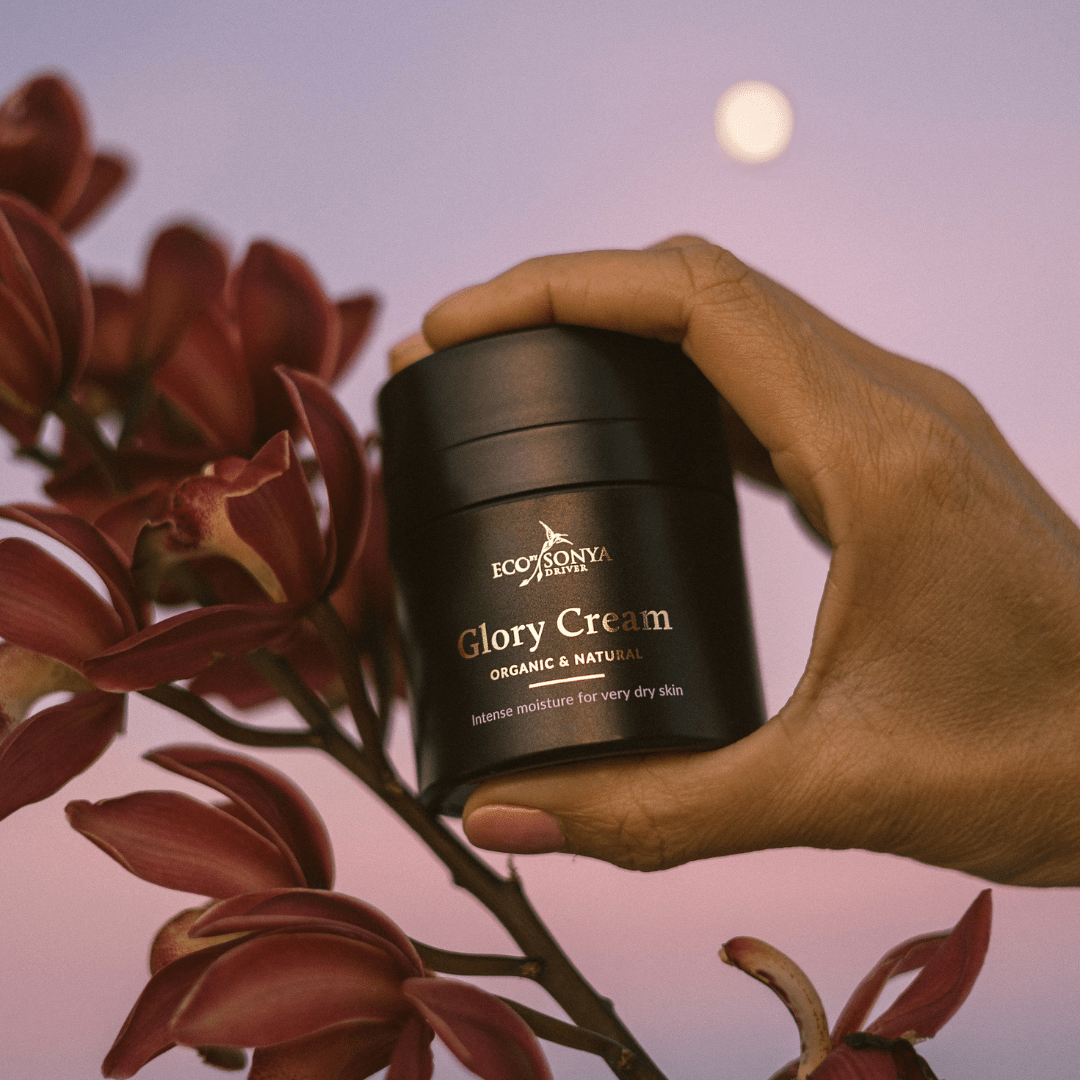 Hand holding a jar of Eco by Sonya Glory Cream with flowers in the background