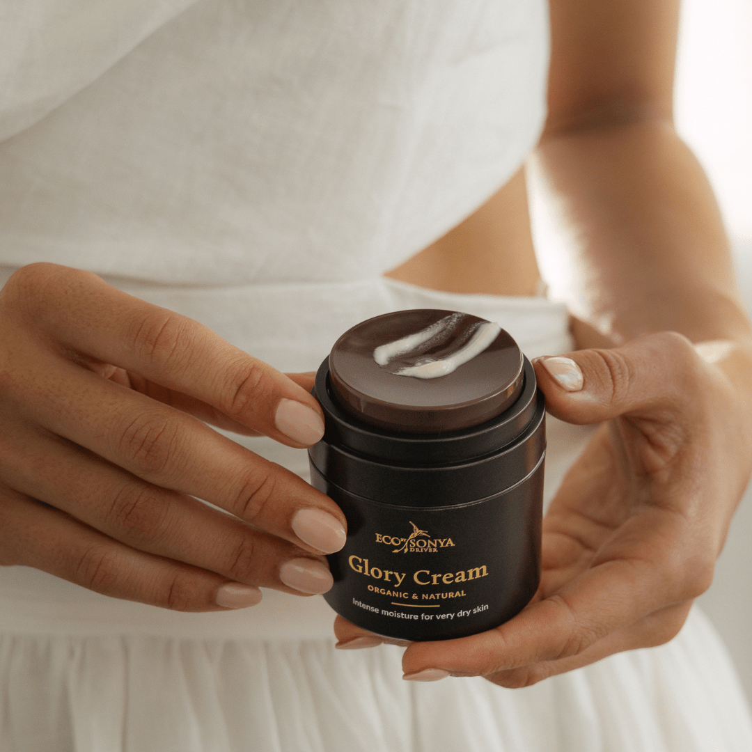 Person holding a jar of natural Glory Cream with a white background with cream smear