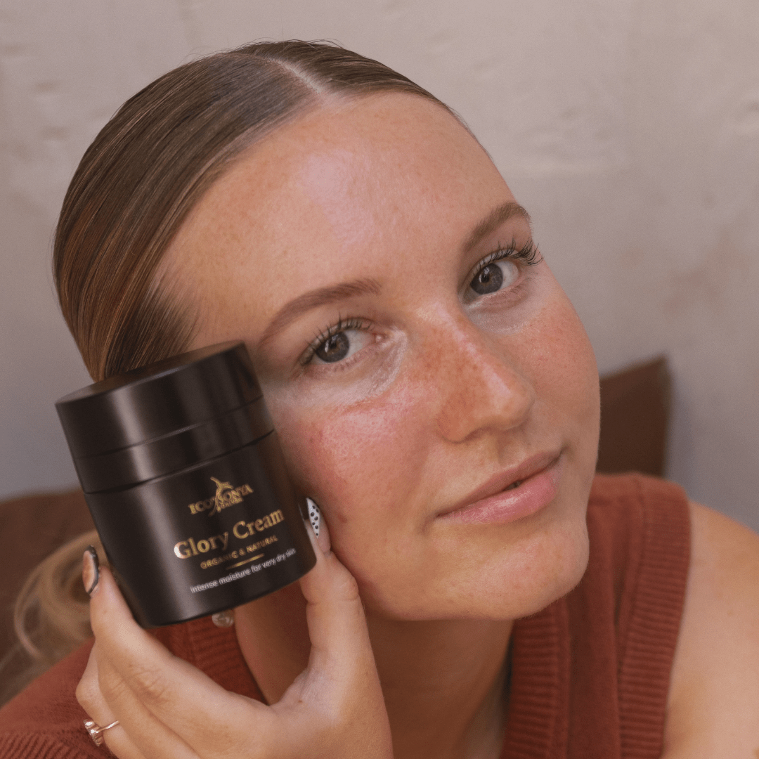Woman holding a jar of 'Glory Cream' close to her face against a neutral background