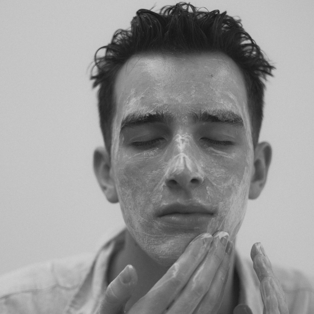 Black and white photo of a person applying Super Citrus Cleanser to their face with a neutral background