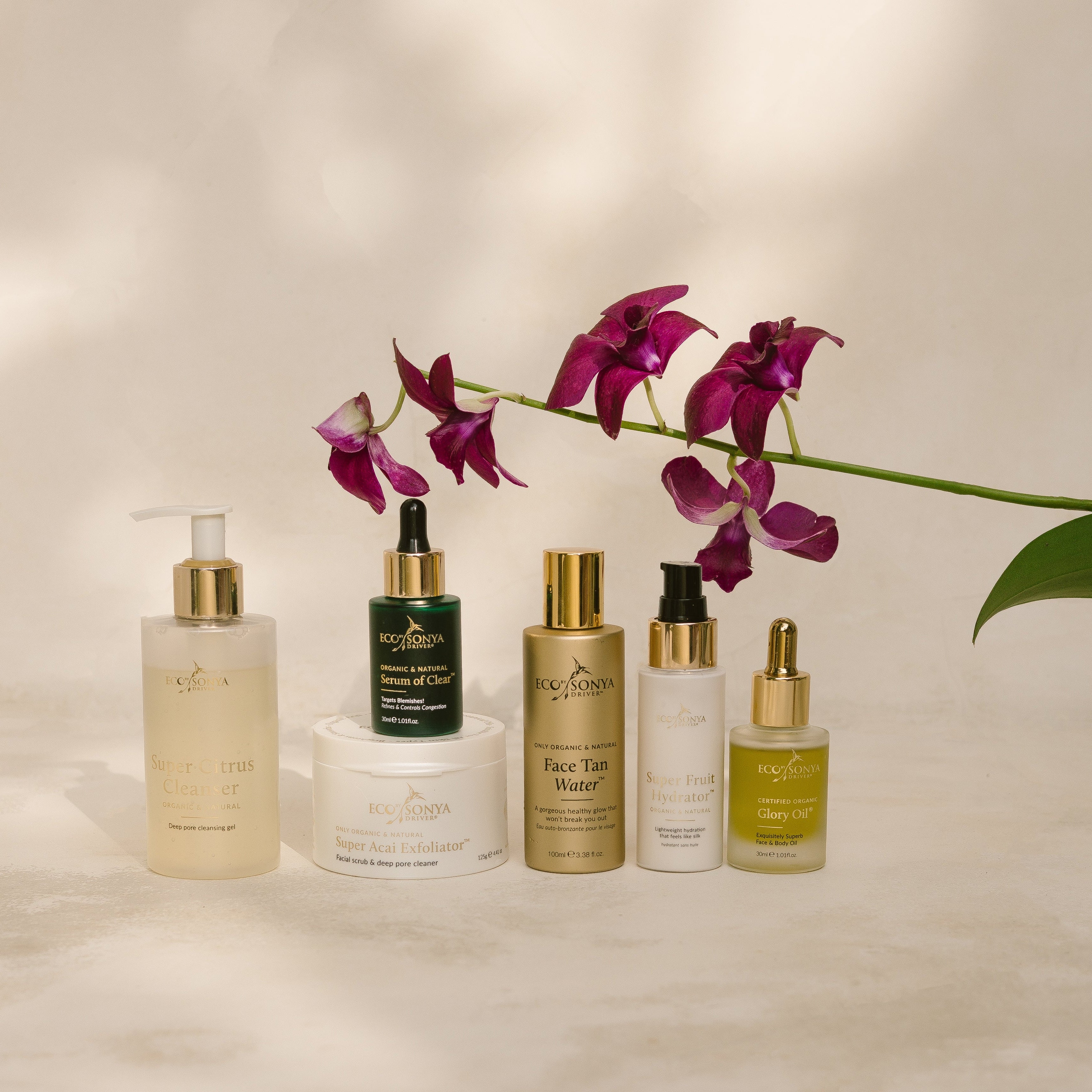 Set of Eco By Sonya skincare products with a purple orchid on a neutral background
